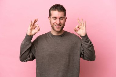 Zen pozisyonunda pembe arka planda izole edilmiş genç beyaz bir adam.