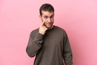 Pembe arka planda izole edilmiş genç beyaz bir adam bir şey gösteriyor.