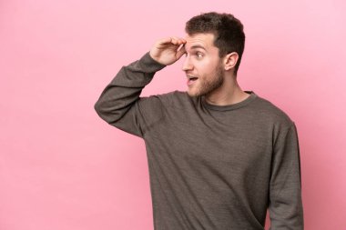 Pembe arka planda mahsur kalmış beyaz bir genç. Sürpriz bir ifadeyle yan tarafa bakıyor.