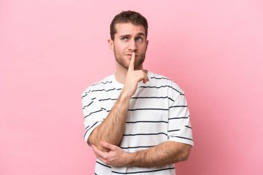 Pembe arka planda izole edilmiş genç beyaz adam yukarı bakarken şüphe duyuyor.