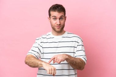 Pembe arka planda izole genç beyaz adam geç kalma jesti yapıyor.