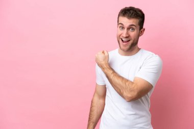 Pembe arka planda izole edilmiş genç beyaz bir adam zaferi kutluyor.