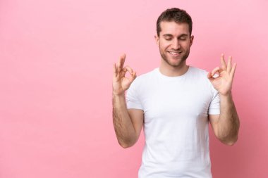 Zen pozisyonunda pembe arka planda izole edilmiş genç beyaz bir adam.