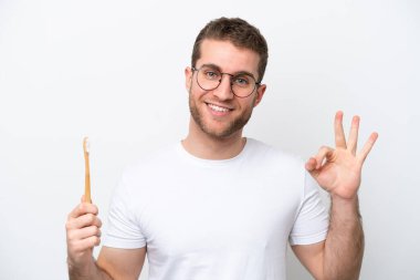 Young caucasian woman brushing teeth isolated on white background showing ok sign with fingers