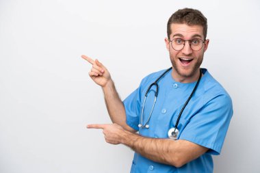 Young surgeon doctor caucasian man isolated on white background surprised and pointing side
