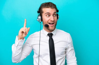 Telemarketer caucasian man working with a headset isolated on blue background intending to realizes the solution while lifting a finger up