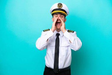 Kafkasyalı pilot mavi arka planda izole edilmiş bağırıyor ve bir şey duyuruyor.