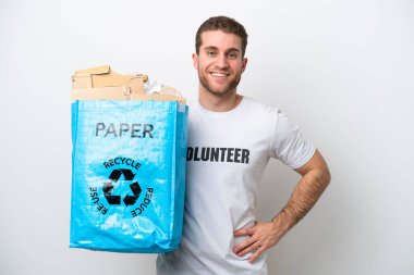 Beyaz arka planda izole edilmiş, kolları kalçasında poz veren ve gülümseyen, geri dönüşüm kağıdı dolu bir çanta tutan beyaz bir adam.