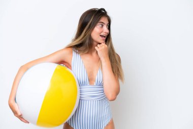 Young woman in swimsuit holding beach ball isolated on white background thinking an idea and looking side