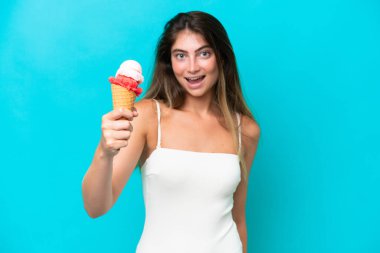 Young woman in swimsuit holding an ice cream isolated on blue background with happy expression