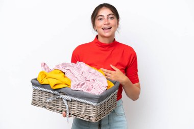 Young caucasian woman holding a clothes basket isolated on white background smiling a lot