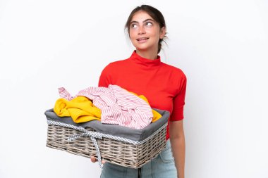 Young caucasian woman holding a clothes basket isolated on white background thinking an idea while looking up