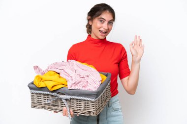 Young caucasian woman holding a clothes basket isolated on white background saluting with hand with happy expression