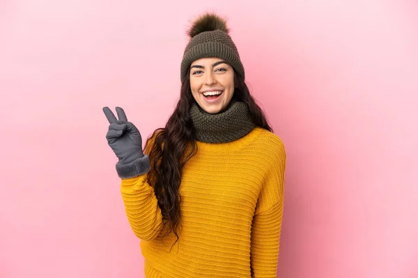 年轻的高加索女孩 头戴冬季帽 背景为紫色 面带微笑 显示出胜利的迹象 — 图库照片