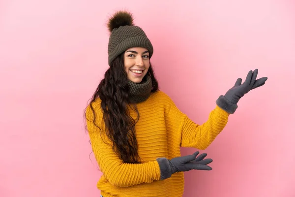 年轻的高加索女孩 头戴紫色背景的冬帽 向旁边伸出手来 邀请她来 — 图库照片
