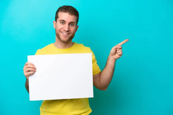 Jovem Caucasiano Isolado Fundo Azul Segurando Cartaz Vazio Apontando Lado — Fotografia de Stock