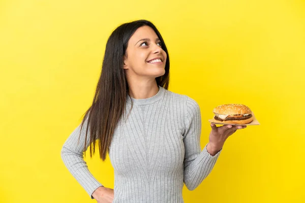Young Caucasian Woman Holding Burger Isolated Yellow Background Thinking Idea — Stock Photo, Image