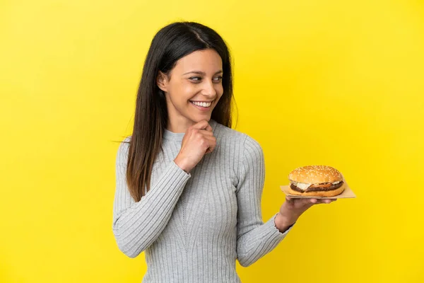 Young Caucasian Woman Holding Burger Isolated Yellow Background Looking Side — Stock Photo, Image