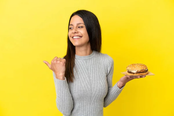 Young Caucasian Woman Holding Burger Isolated Yellow Background Pointing Side — Stock Photo, Image