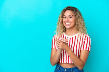 Kıvırcık saçlı kız mavi arka planda yalnız gülüyor.