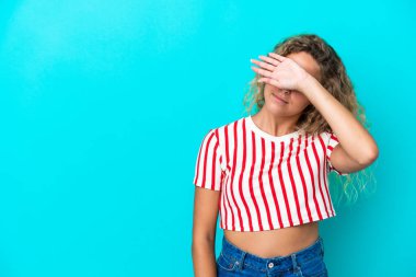 Kıvırcık saçlı kız mavi arka planda tek başına gözlerini elleriyle kapatıyor.