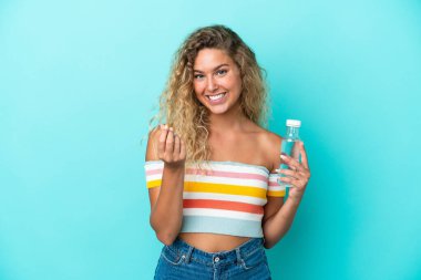 Mavi arka planda su şişesi olan genç sarışın kadın para hareketi yapıyor.