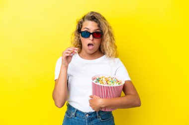 Sarı arka planda üç boyutlu gözlüklü ve elinde koca bir kova patlamış mısır tutan kıvırcık saçlı kız.