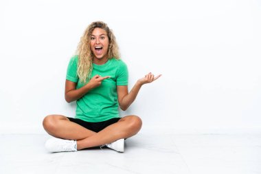 Yerde oturan kıvırcık saçlı kız şaşırmış ve işaret ediyor.