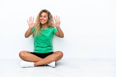 Girl with curly hair sitting on the floor counting nine with fingers