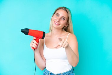 Mavi arka planda saç kurutma makinesini tutan beyaz bir kadın kendine güvenen bir ifadeyle seni işaret ediyor.