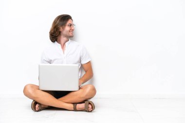 Young handsome man with a laptop sitting on the floor isolated on white background in lateral position