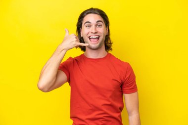 Caucasian handsome man isolated on yellow background making phone gesture. Call me back sign
