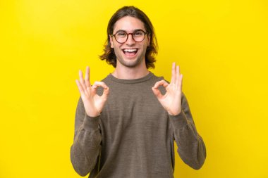 Caucasian handsome man isolated on yellow background showing ok sign with two hands