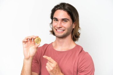 Young handsome man holding a Bitcoin isolated on white background and pointing it