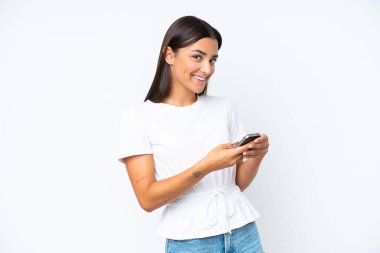 Beyaz arka planda izole edilmiş genç beyaz kadın cep telefonuyla mesaj gönderiyor.