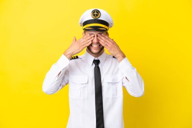 Airplane caucasian pilot isolated on yellow background covering eyes by hands