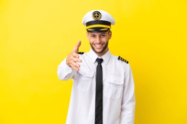 Airplane caucasian pilot isolated on yellow background shaking hands for closing a good deal