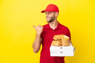 Pizza teslimatçısı, izole edilmiş arka planda pizza kutularını ve hamburgerleri topluyor. Ürünü sunmak için yan tarafa bakıyor.