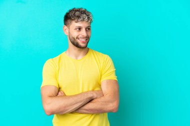 Mavi arka planda izole edilmiş yakışıklı beyaz adam mutlu ve gülümsüyor.