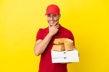 pizza delivery man picking up pizza boxes and burgers over isolated background happy and smiling