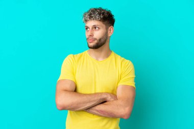 Mavi arka planda izole edilmiş yakışıklı beyaz adam yan tarafa bakıyor.