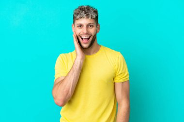 Mavi arka planda mahsur kalmış yakışıklı beyaz adam şaşırmış ve şok olmuş bir yüz ifadesi var.