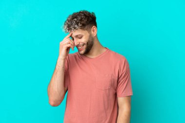 Mavi arka planda izole edilmiş yakışıklı beyaz adam gülüyor.