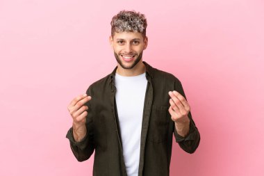 Young handsome caucasian man isolated on pink background making money gesture