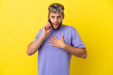 Young caucasian man using mobile phone isolated on yellow background surprised and shocked while looking right
