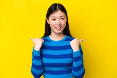 Young Chinese woman isolated on yellow background with thumbs up gesture and smiling
