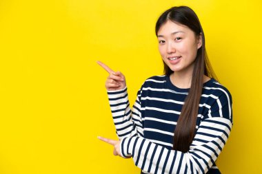 Young Chinese woman isolated on yellow background pointing finger to the side and presenting a product