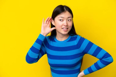 Sarı arka planda izole edilmiş genç bir Çinli kadın bir şeyler dinliyordu. Elini kulağına koyarak.