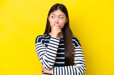 Young Chinese woman isolated on yellow background having doubts and with confuse face expression