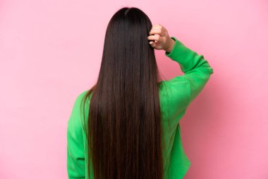 Young Chinese woman isolated on pink background in back position and thinking
